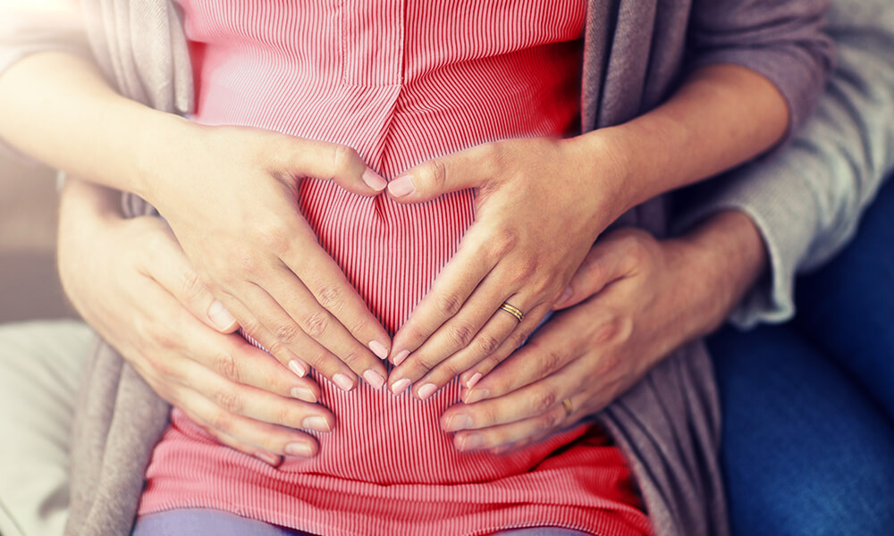 Two sets of hands creating a heart shape on a baby bump