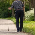 An elderly man walking on a path with walking sticks